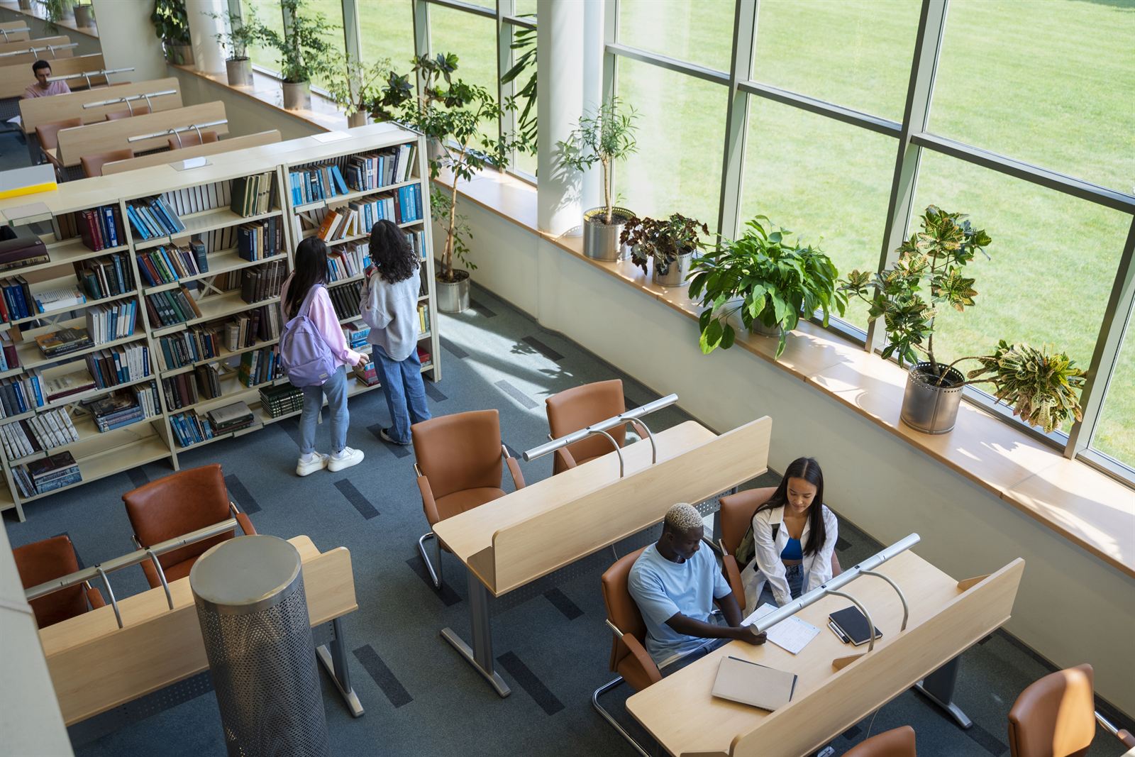 Students browsing bookshelves and studying together in a bright library.