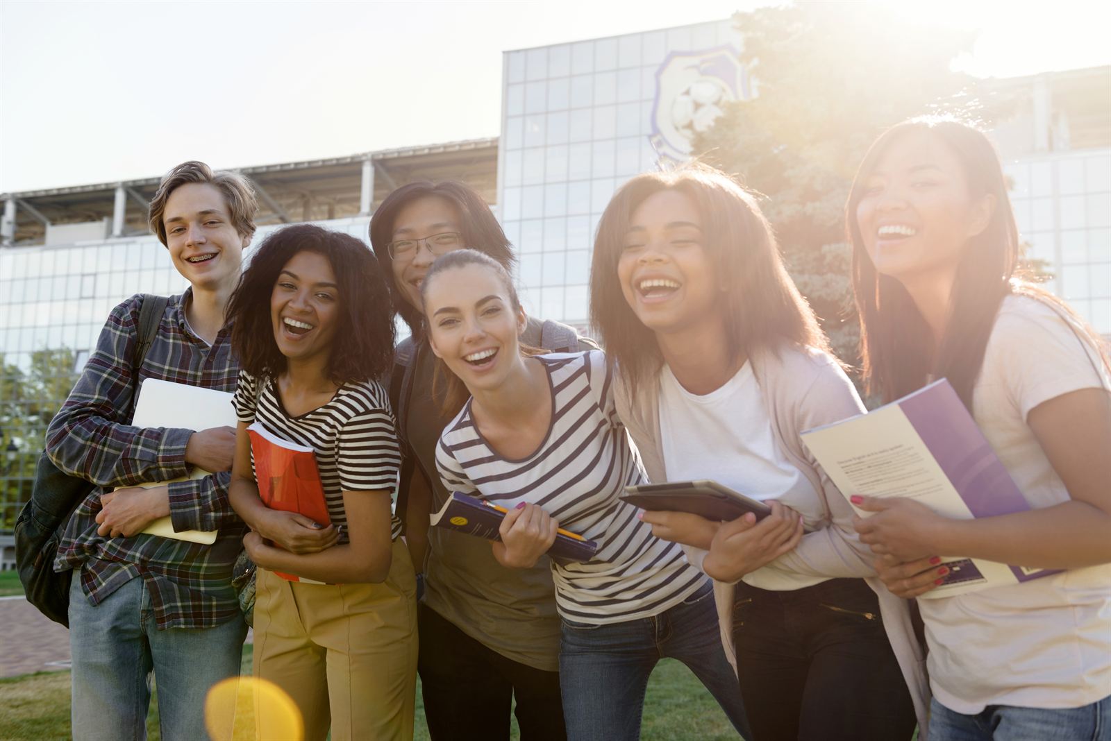 A diverse group of cheerful students laughing together outdoors in the sunshine.