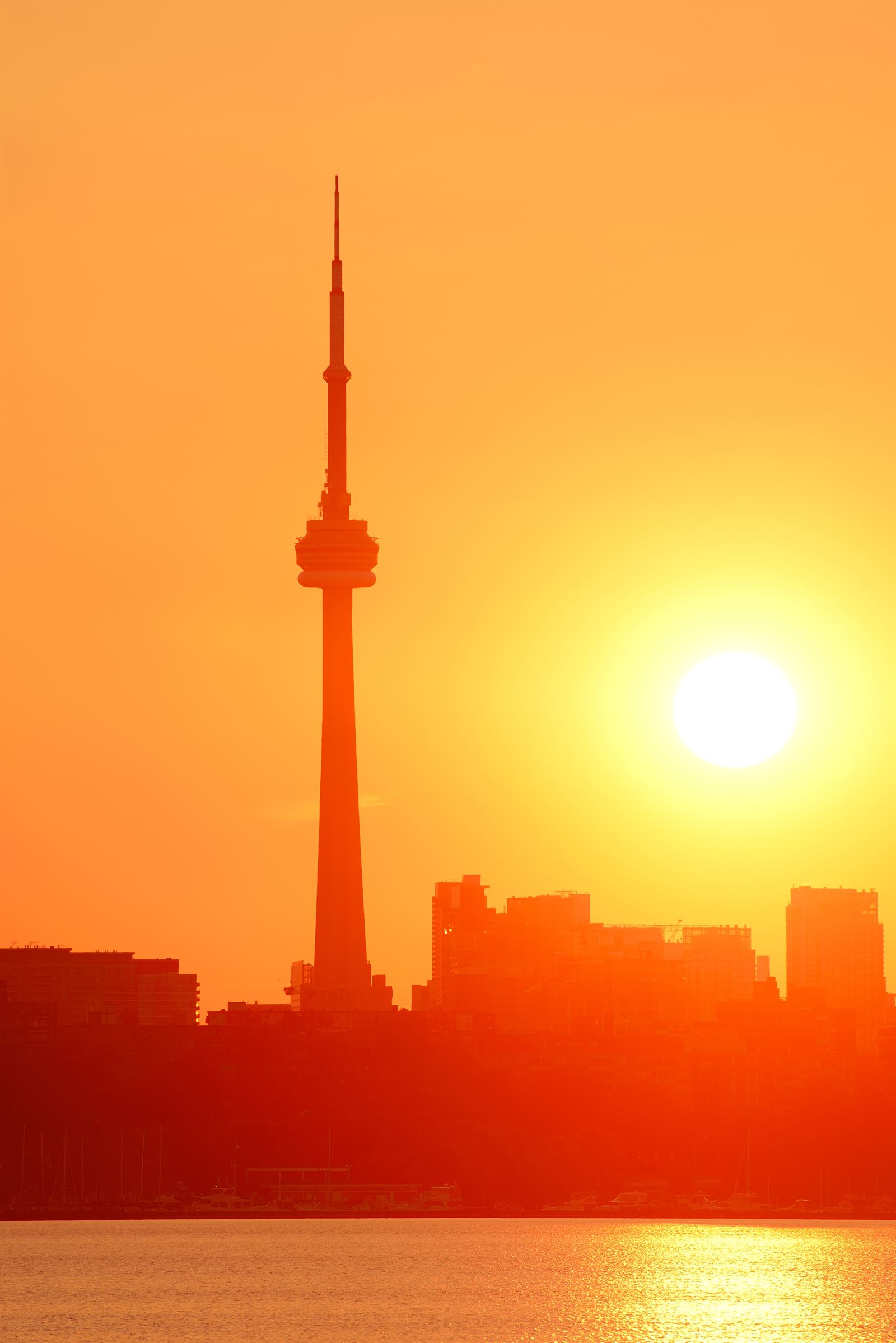 The Toronto skyline and CN Tower in silhouette against a bright orange sunrise over Lake Ontario.